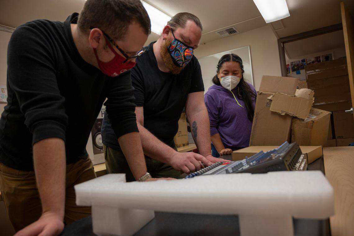 Patrick Doran, left, a student wellness coordinator; Justin Aceveda, a student at Northwest Indian College; and Gaby Salazar, a communications faculty member of the college, unbox a new audio mixer the school’s music club received through a grant on Tuesday, April 5, in Whatcom County.