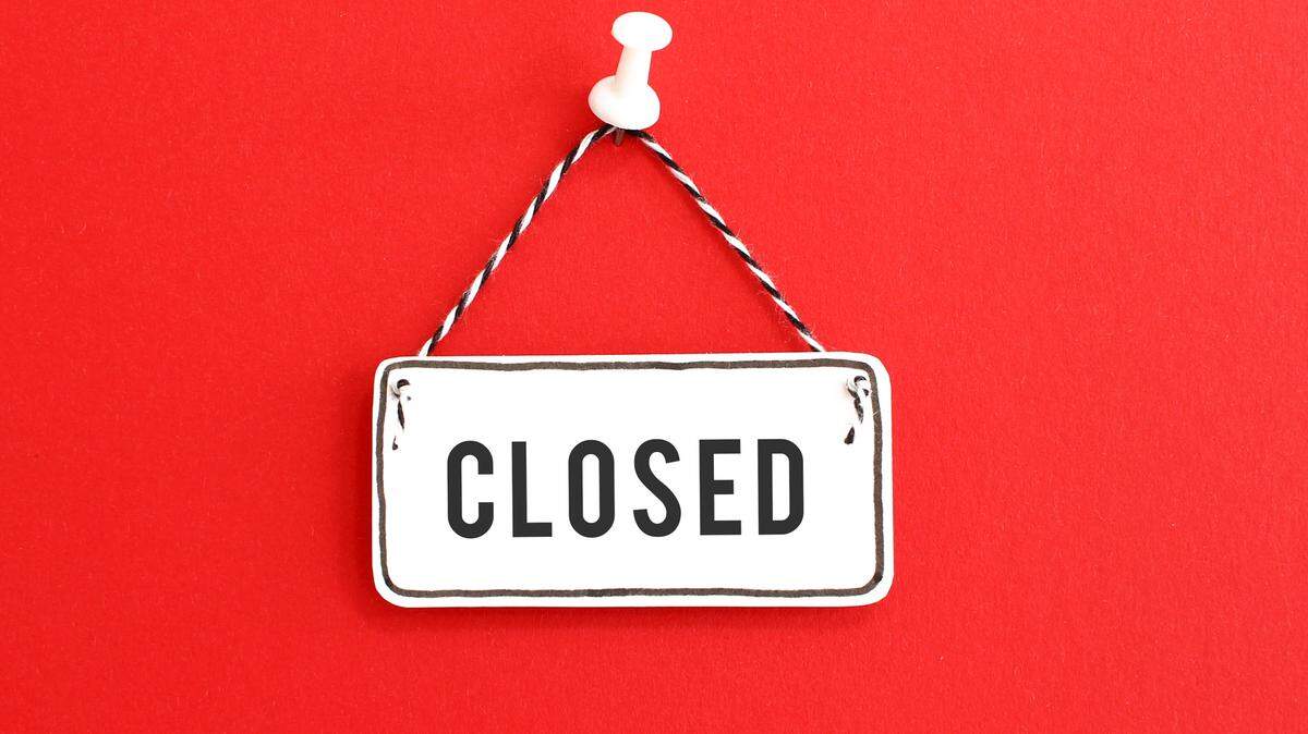 Handmade signboard with Closed inscription and striped rope hanging on pin on bright red background.