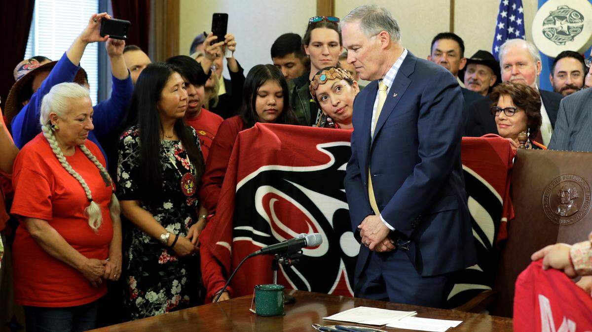 Washington Gov. Jay Inslee is presented with an honoring blanket held by Earth Feather Sovereign, center- left, of the Confederated Tribes of the Colville Reservation, after Inslee signed a bill into law April 24 in Olympia. The bill creates liaison positions within the Washington State Patrol, and requires the agency to develop best practices in hopes of reducing disproportionate rates of violence faced by Native American and indigenous women, and also the frequency with which perpetrators of the crimes avoid justice.