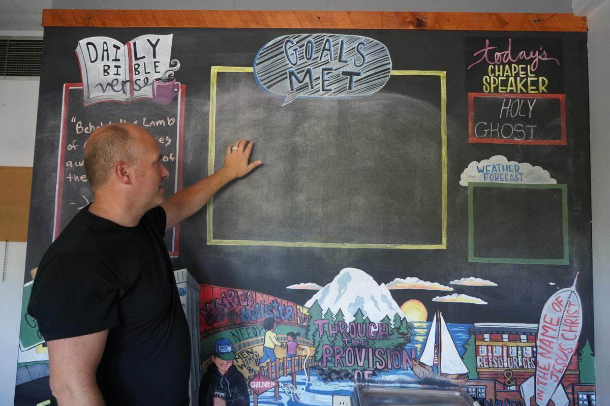 Lighthouse Mission Ministries President and CEO Hans Erchinger-Davis gestures to a chalkboard used for homeless services in the old Mission building at 910 Holly St. on Monday, Oct. 3, in Bellingham.