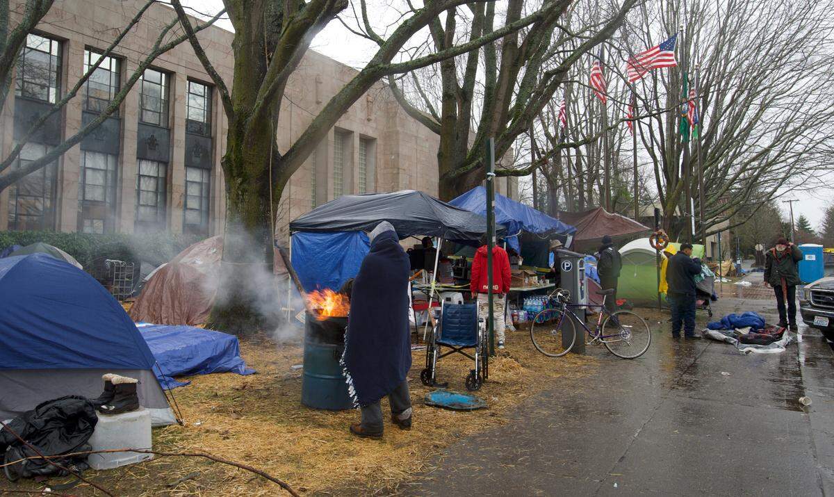 A person without housing stands next to a fire at an encampment in front of Bellingham City Hall on Wednesday, Dec. 9.