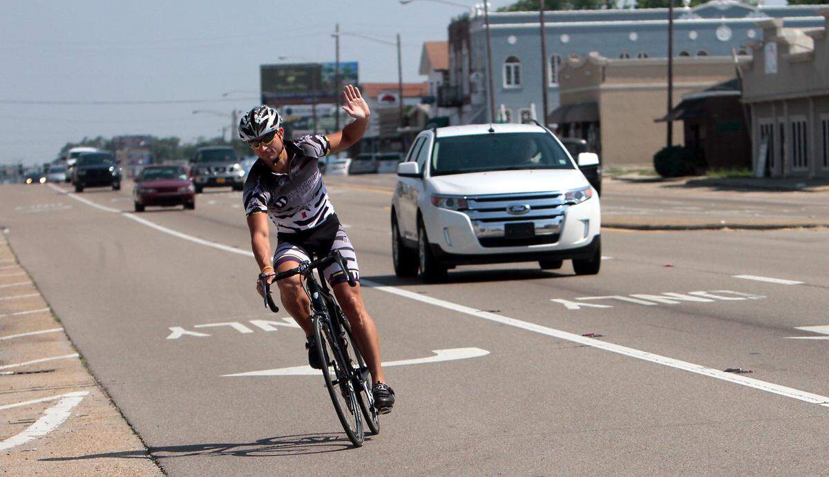AMANDA McCOY/SUN HERALD Justin Ford demonstrates how to signal a right turn while riding his bicycle on U.S. 40 on Friday, May 18 2012. May is National Bicycle Month.