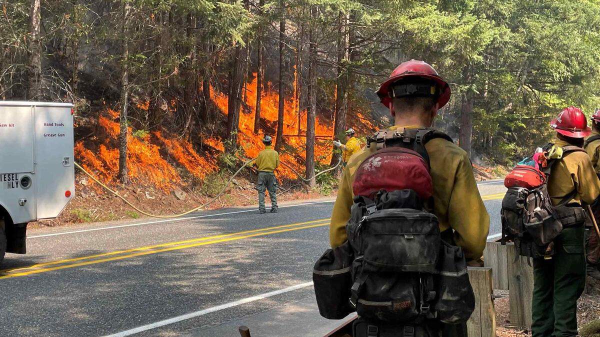Firefighters douse flames along state Highway 20 near Newhalem, Wash., on Monday, Aug. 14, 2023.