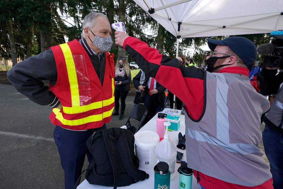 Washington Gov. Jay Inslee, left, has his temperature taken at an entrance station, Thursday, March 4, during a visit to a drive-up mass vaccination site in Puyallup. Officials said they expected to deliver approximately 2,500 second doses of the Moderna COVID-19 vaccine at the site Thursday.