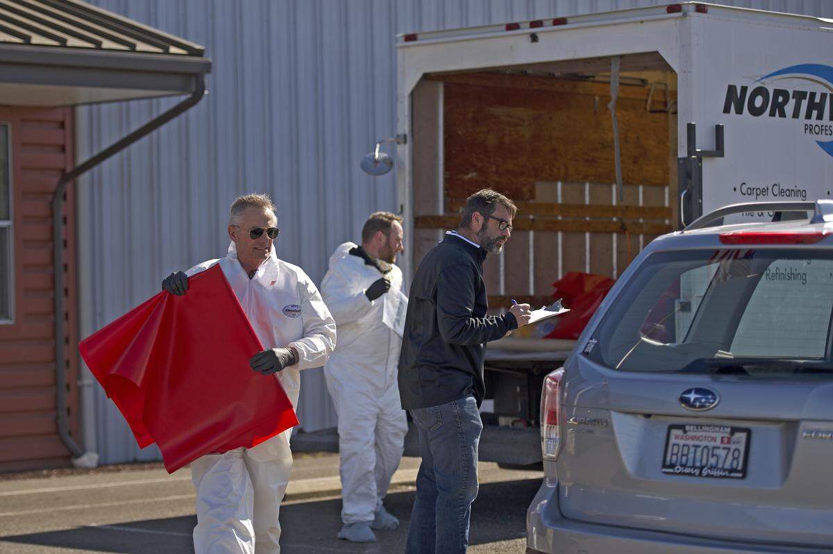 Doug Broersma, founder of Northwest Professional Services, loads a vinyl template used for making cots into a volunteer’s car while Brian Davidson, CEO of Christensen Net Works, speaks to the volunteer on April 1 in Everson. Christensen Net Works has begun retooling its facility to make 200 cots a day for healthcare agencies during the coronavirus pandemic.