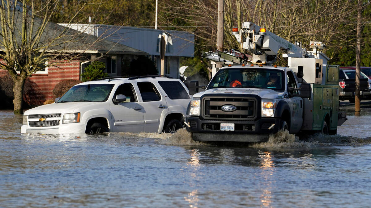 A worker in a truck drives by a vehicle stuck in floodwater on a road Wednesday, Nov. 17, 2021, in Sumas, Wash. 