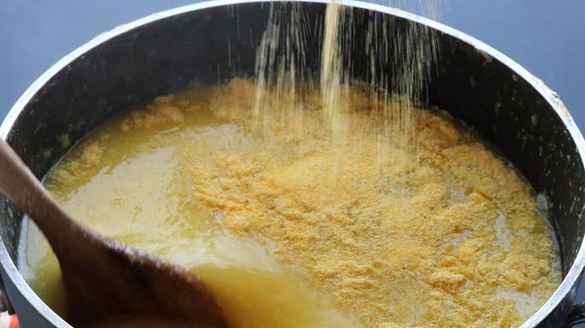 Polenta is sprinkled into a pot of boiling water while stirring briskly.
