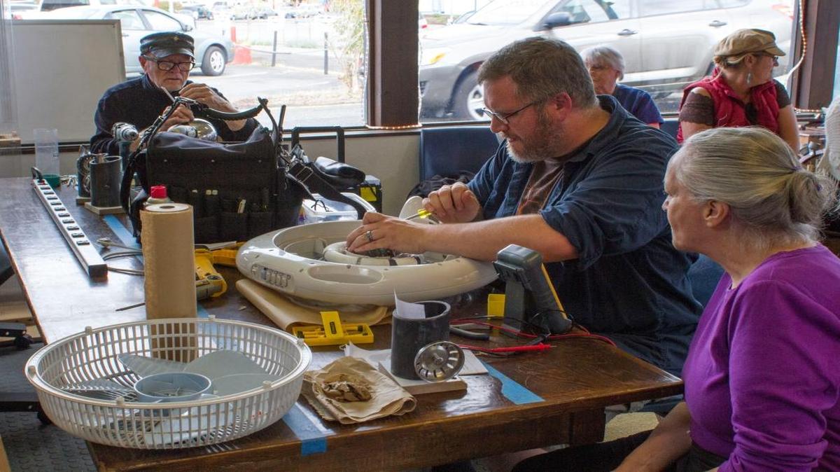 Chuck Creswell, left, Brendon Orth-Sheridan and Linda Joy attend the first Bellingham Repair Cafe on Sept. 6, 2015. Joy watches as Orth-Sheridan checks the motor of her broken fan while Creswell fixes her broken colander.