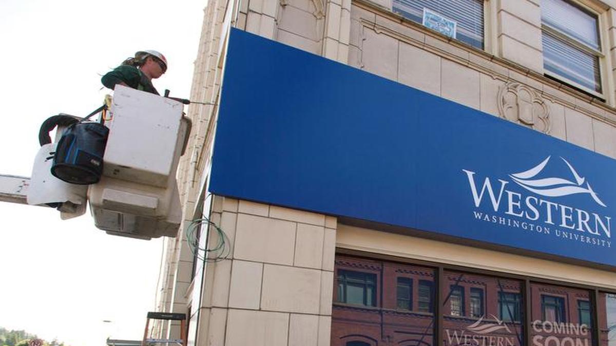 
Sam Jones of The Sign Post installs a large Western Washington University sign on the corner of the Herald Building in June 2015.
