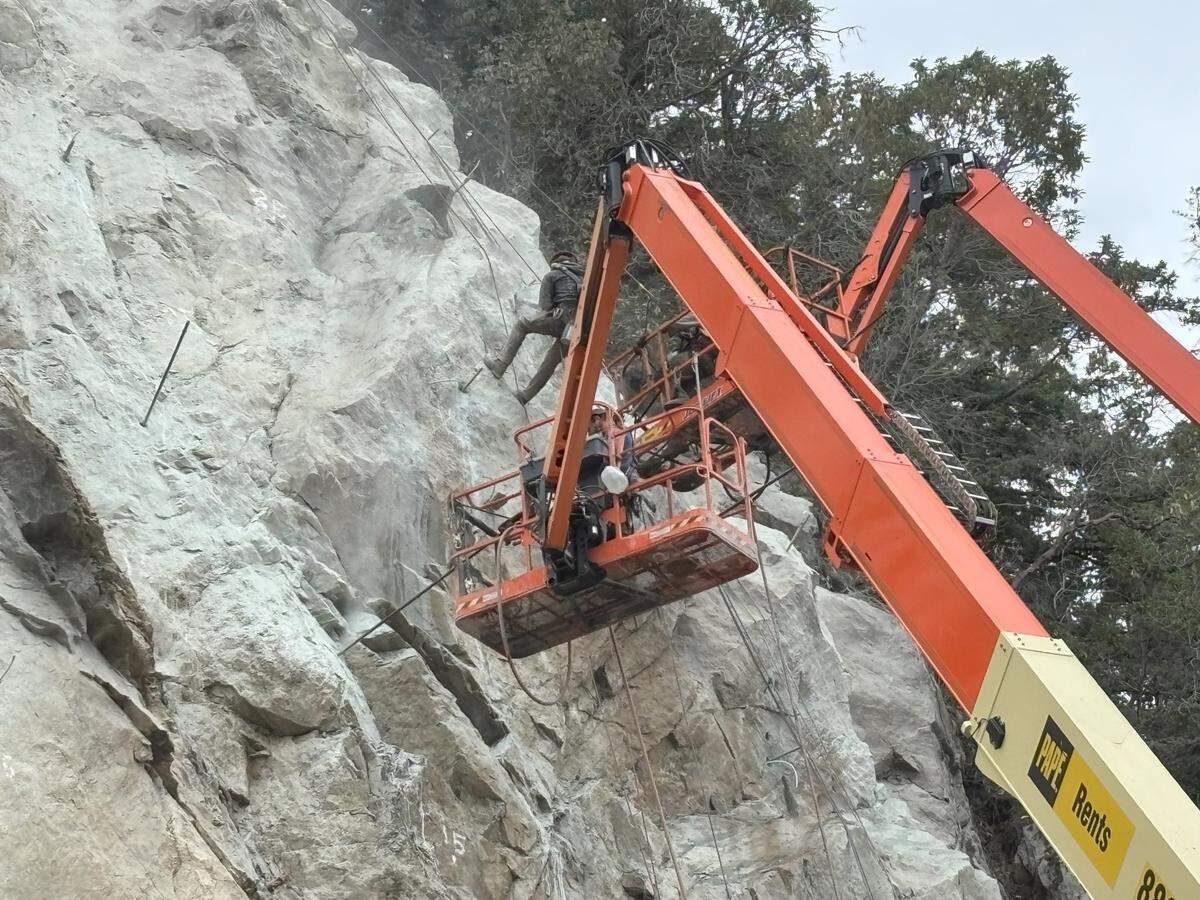 One worker descends down the cliff while two others work from separate baskets. They are drilling holes into the cliff face to attach rock bolts and hold the cliff together. About 50 rock bolts are being installed.
