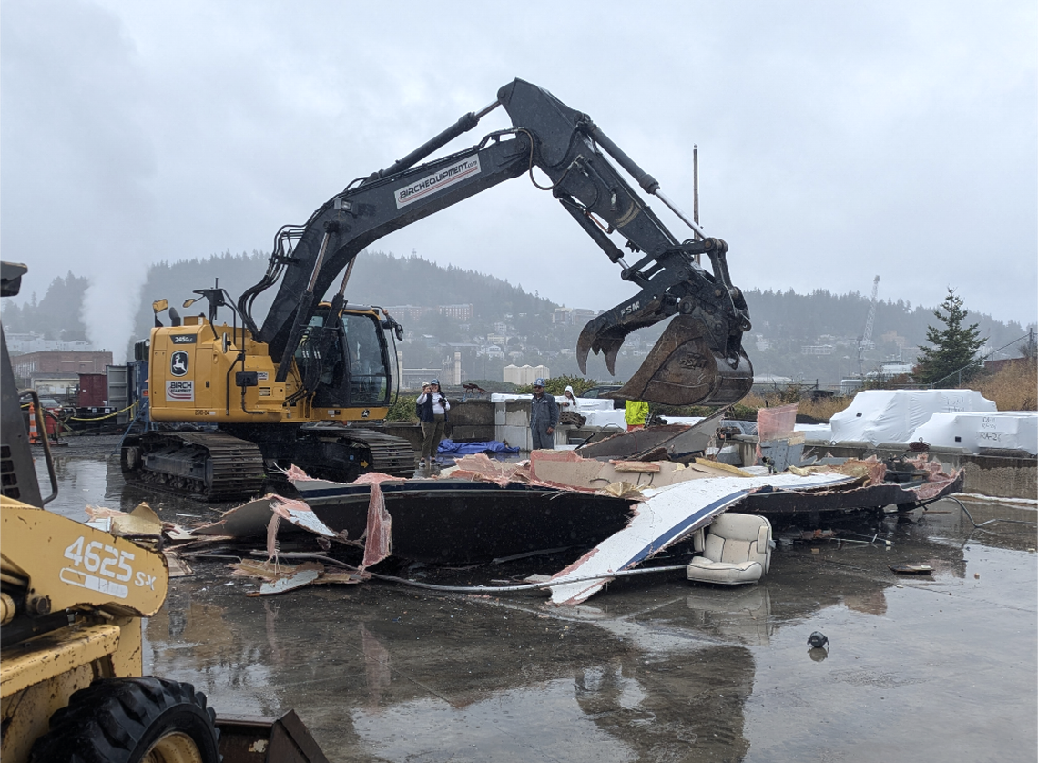 An excavator rips apart a derelict boat that could cause a safety hazard if left in the water.