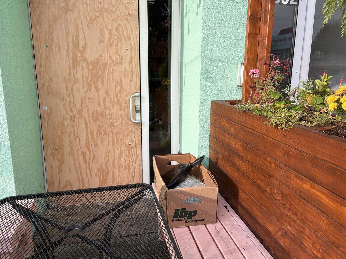 A bin of swept-up glass shards sits outside the boarded-up door of L&L Libations in Bellingham following a break-in.