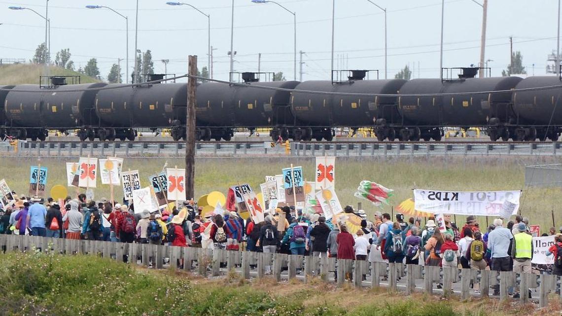 In this May 14, 2016, photo, anti-oil protestors walk past the Tesoro refinery rail yard in Anacortes. The Justice Department and the Environmental Protection Agency on Monday, July 18, 2016, announced a $425 million settlement with Tesoro Corp. and Par Hawaii Refining to reduce air pollution at six petroleum refineries in the West.