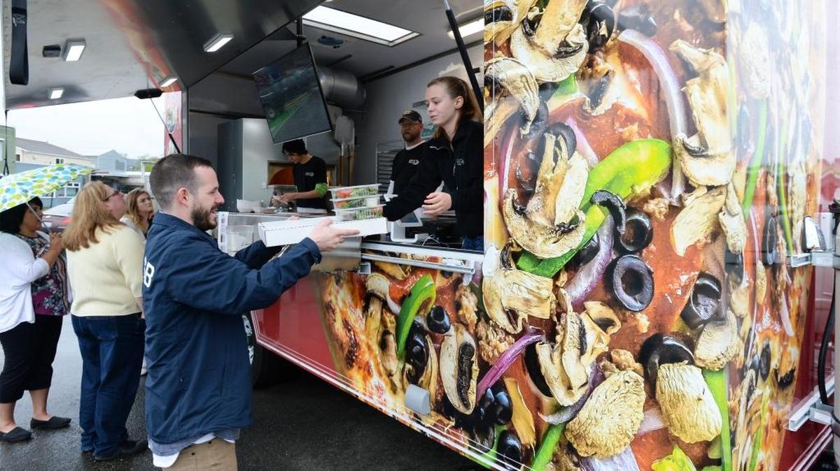 Chas Malich, owner of Chazzam Signs and Graphics, gets pizza from Kara Knopek at the new Pizza’zza food trailer parked on Cornwall Avenue in Bellingham on Thursday, April 14, 2016. Chazzam did the graphics on the trailer.