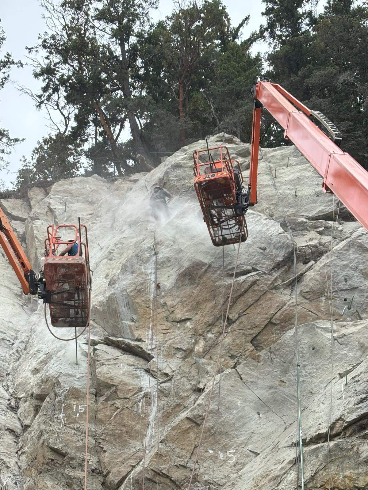 Workers use man lifts on cranes to install rock bolts into the cliff side at Chuckanut Drive June 12.