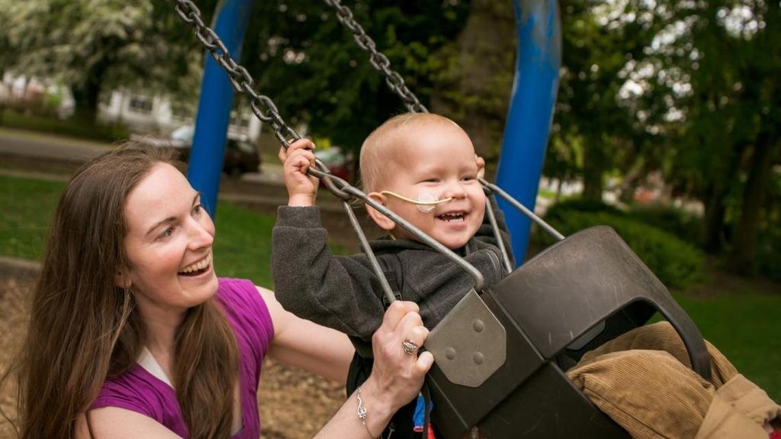 Bellingham resident Lauren Beven pushes son Tristan Wypych in a swing at Elizabeth Park in May. Now 2 1/2 years old, the boy is recovering from a rare brain and spinal cancer. The family is worried about losing the pre-existing condition protection under the Affordable Care Act.