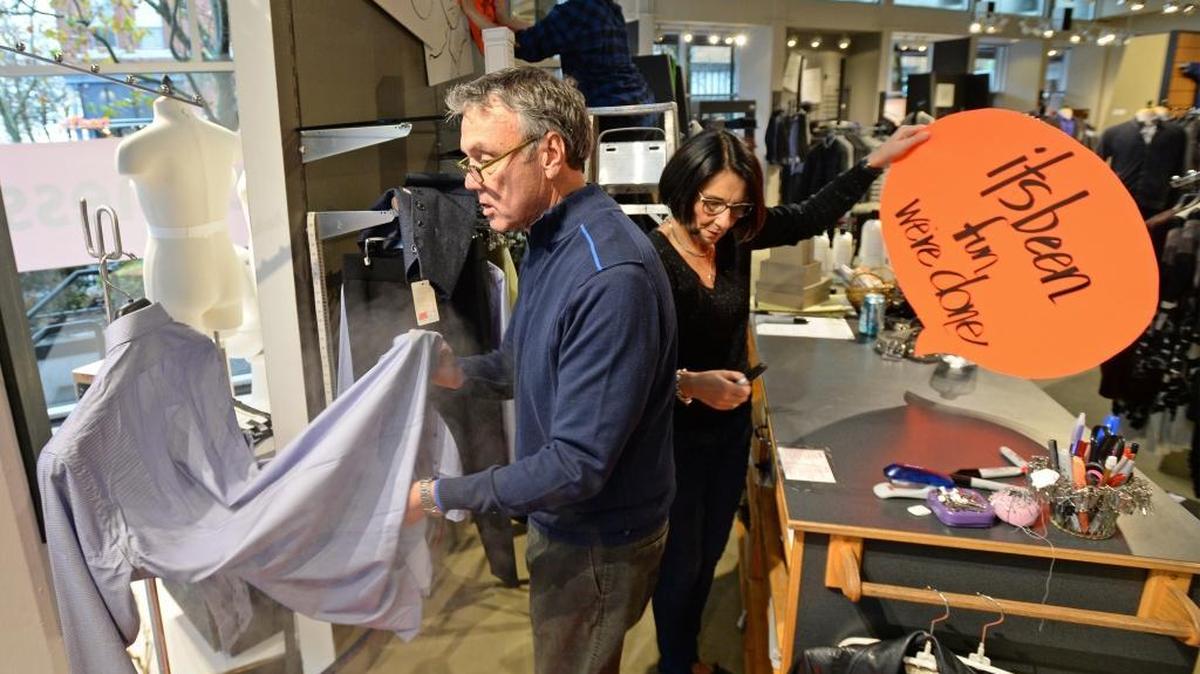 Gary Lupo steams a shirt, his wife Barb Lupo makes going out of business signs and store manager Brianne Trafton hangs signs up while they get ready for a liquidation sale at Garys’ Mens & Womens Wear in downtown Bellingham, Monday, Oct. 31, 2016. The Lupos have owned the store for nearly 40 years.