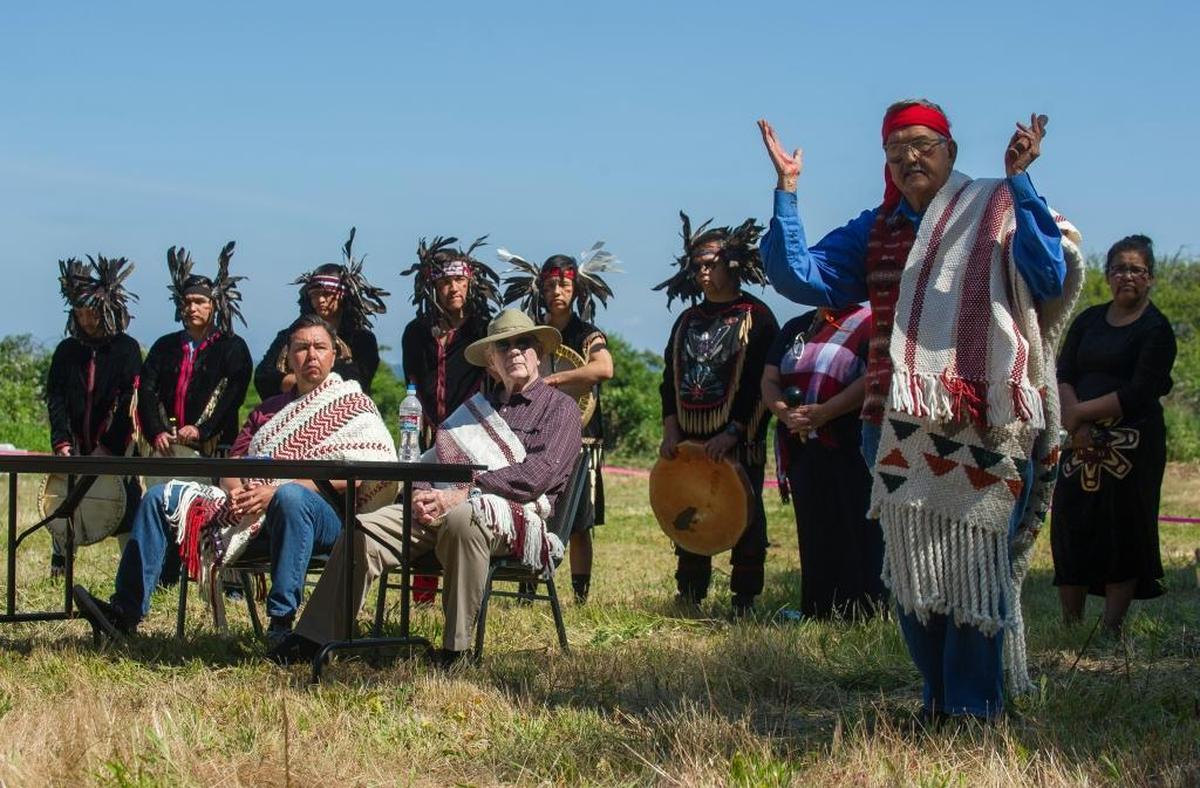 Timothy Ballew II, chairman of Lummi Nation, left, Harry Robinson, mayor of Blaine, center, and Lummi Blackhawk Singers look on as Bill James, Lummi hereditary chief, right, addresses the crowd after nearly 2 acres of burial grounds on Semiahmoo Spit were transferred to Lummi Nation from the City of Blaine on Thursday, June 29.