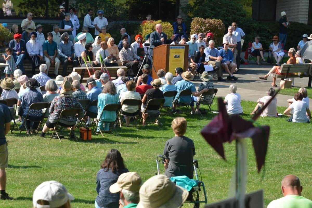 Sheriff Bill Elfo speaks to about 200 people gathered on the lawn behind the Bellingham Public Library during a groundbreaking of the Arch of Healing and Reconciliation. In the foreground is an origami crane, a Japanese symbol of hope and healing.