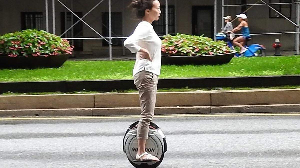 A woman travels down a street on an electric unicycle.