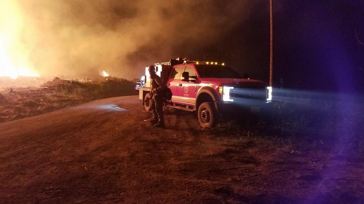 A DNR firefighter is shown next to a wildland fire engine as smoke from the fire rises overnight Sunday on Sumas Mountain.