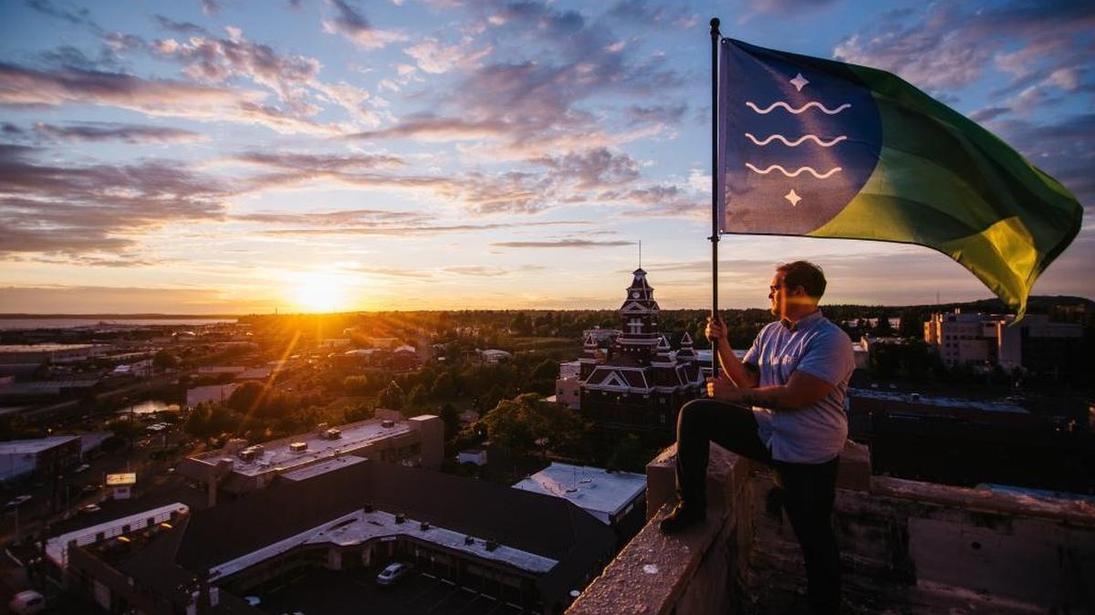 Brad Lockhart, standing on a city rooftop, holds the Bellingham flag he designed.