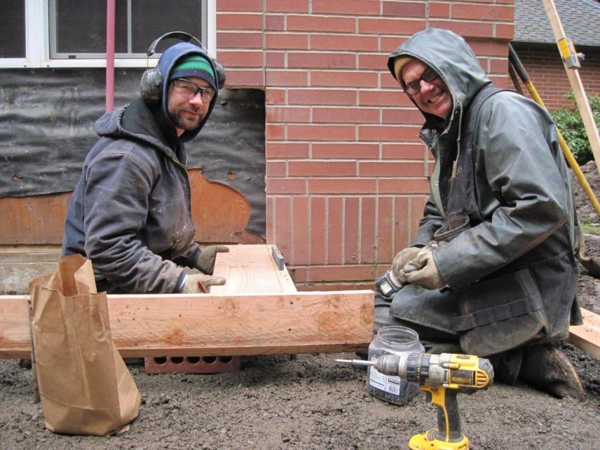 A-1 Builders employees Justin Deane and Mike Gill are at work preparing a brick wall for a new door. A-1 Builders will become a worker-owned cooperative in July.