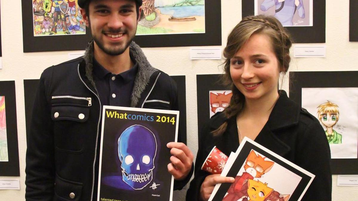 Whatcom County teen artists Abbey Drury and Nirmal Nair stand in front of their art and holding Whatcomics 2014 at the 2014 Teen Art Show.

