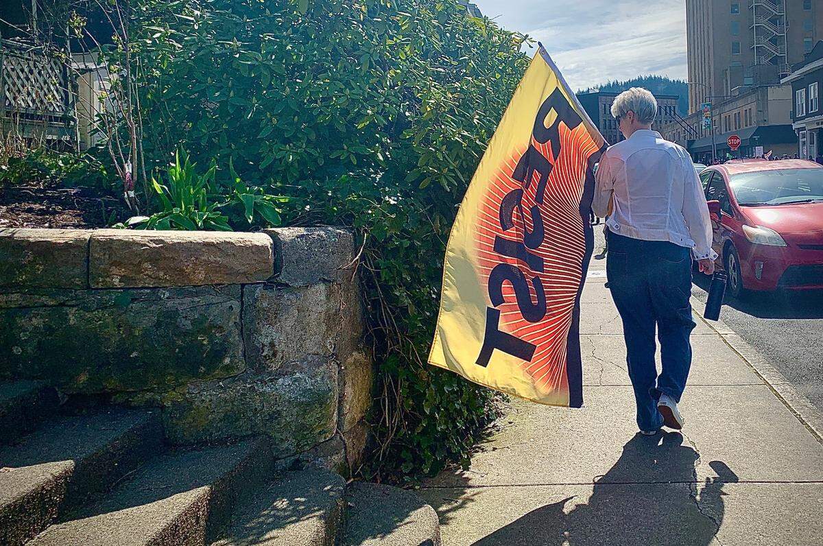 A protest participant walks away from the Hands Off! gathering at Bellingham City Hall with a “Resist” flag in tow.