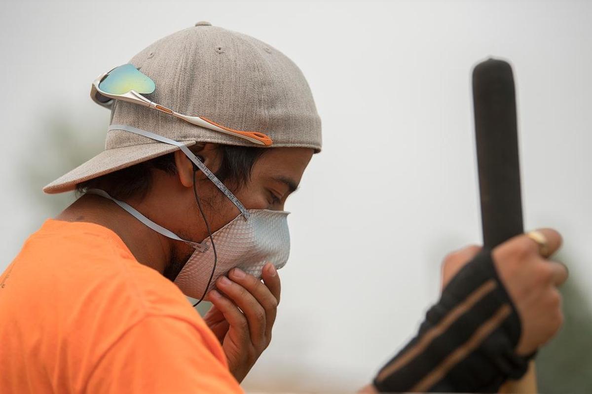 Jonathan Torres, who works at the Clark County Fairgrounds, adjusts his mask while protecting himself from wildfire smoke as he helps clean the stables with colleagues Wednesday morning, Sept. 6, 2017, in Ridgefield, Wash.