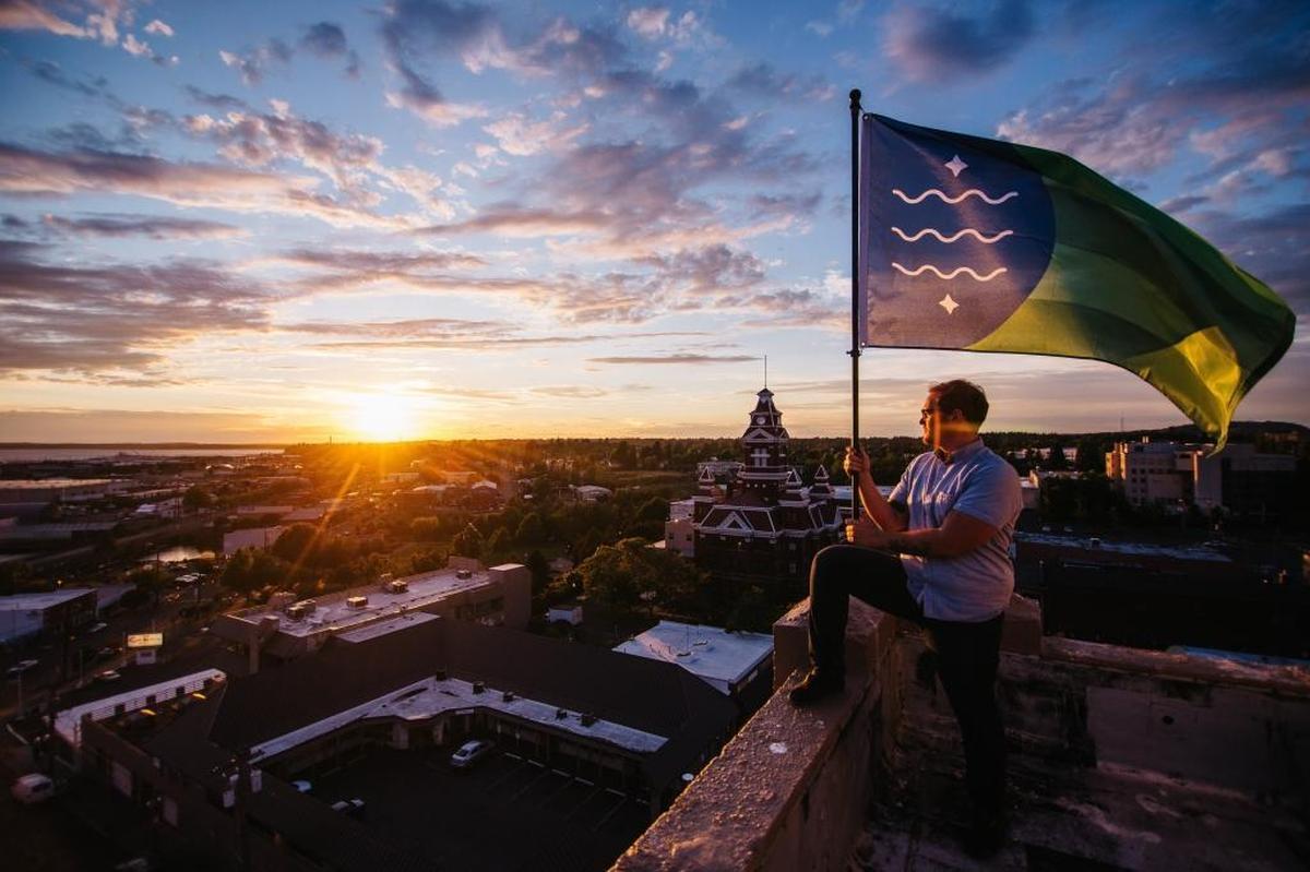 Brad Lockhart holds the Bellingham flag he designed on a city rooftop at sunset.