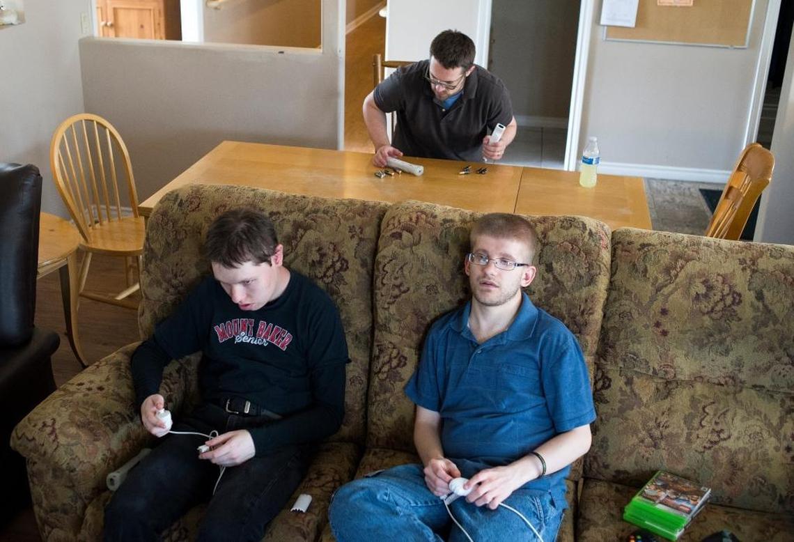 Luke LeViere, program director at Pine Street Home, puts batteries in Nintendo Wii remotes as Allen Turner, left, and Ricky Manwill, right, wait to play a bowling game on Wednesday, May 10, at Pine Street Home in Lynden. Pine Street is a home operated by Cascade Connections for adults with developmental disabilities.