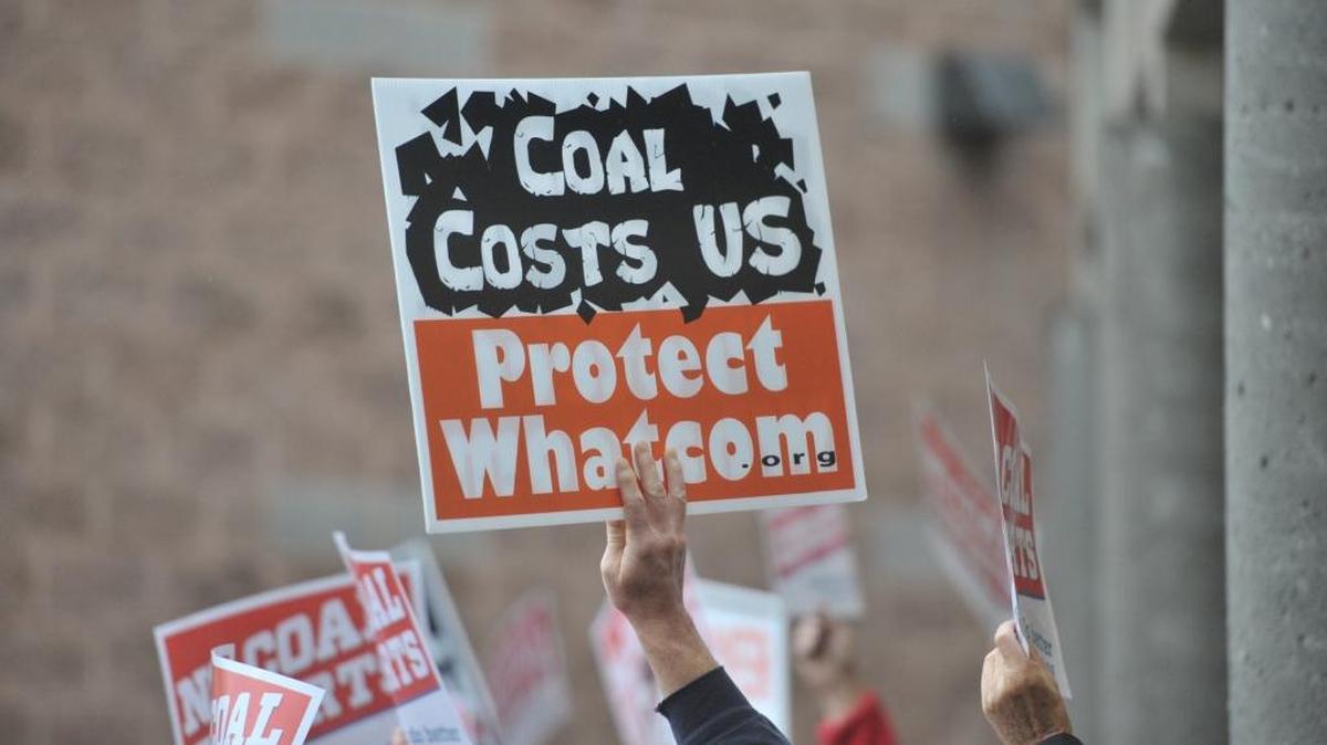 Protesters wave signs at Squalicum High School in October 2012 during a meeting about what needs to be included in an environmental impact study for the proposed Gateway Pacific Terminal. The report is now expected in late 2016.
