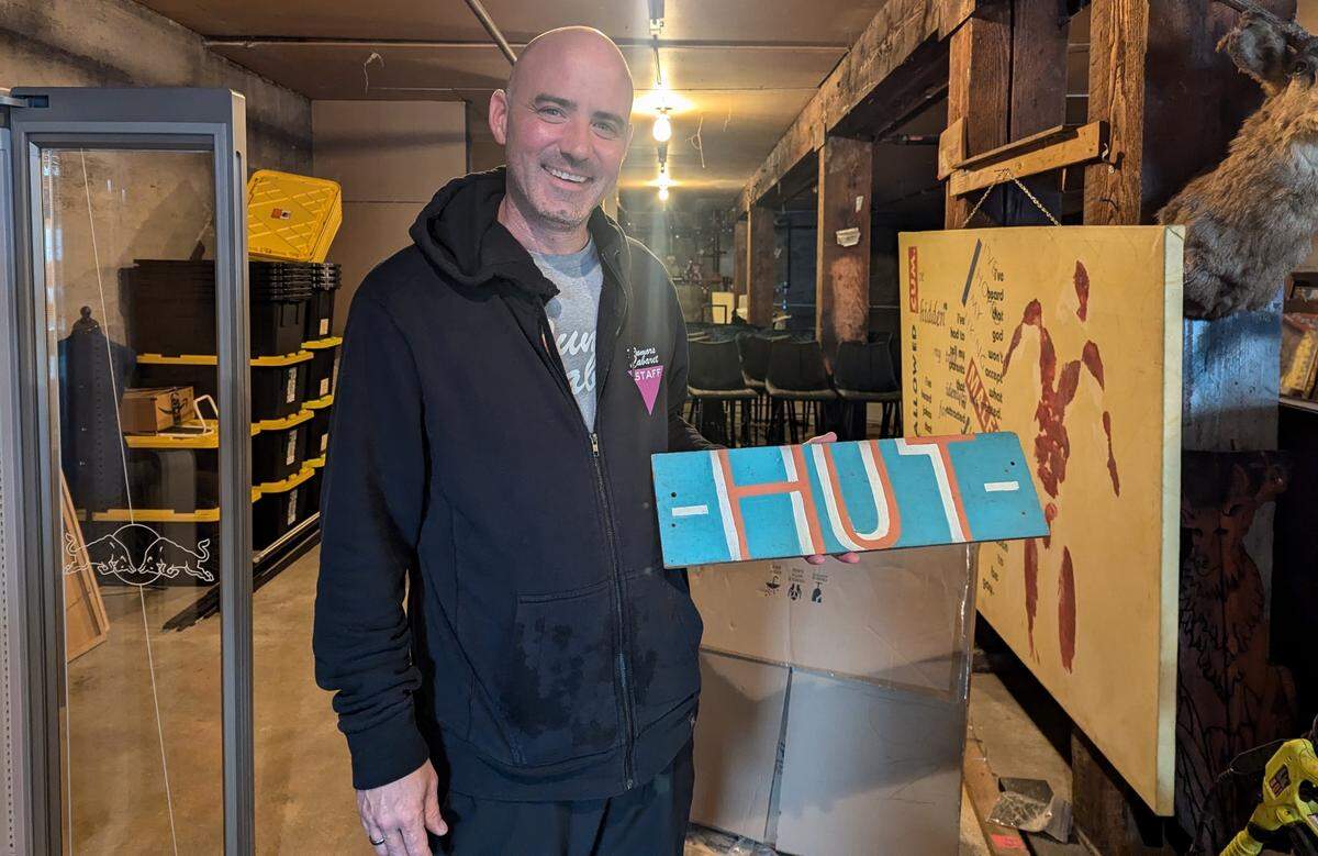 Rian Greer holds up the original sign for The Hut Tavern, a prohibition-era LGBTQ+ venue that would later become Rumors Cabaret. The sign was given to him by a bartender who worked at both The Hut Tavern and Rumors.