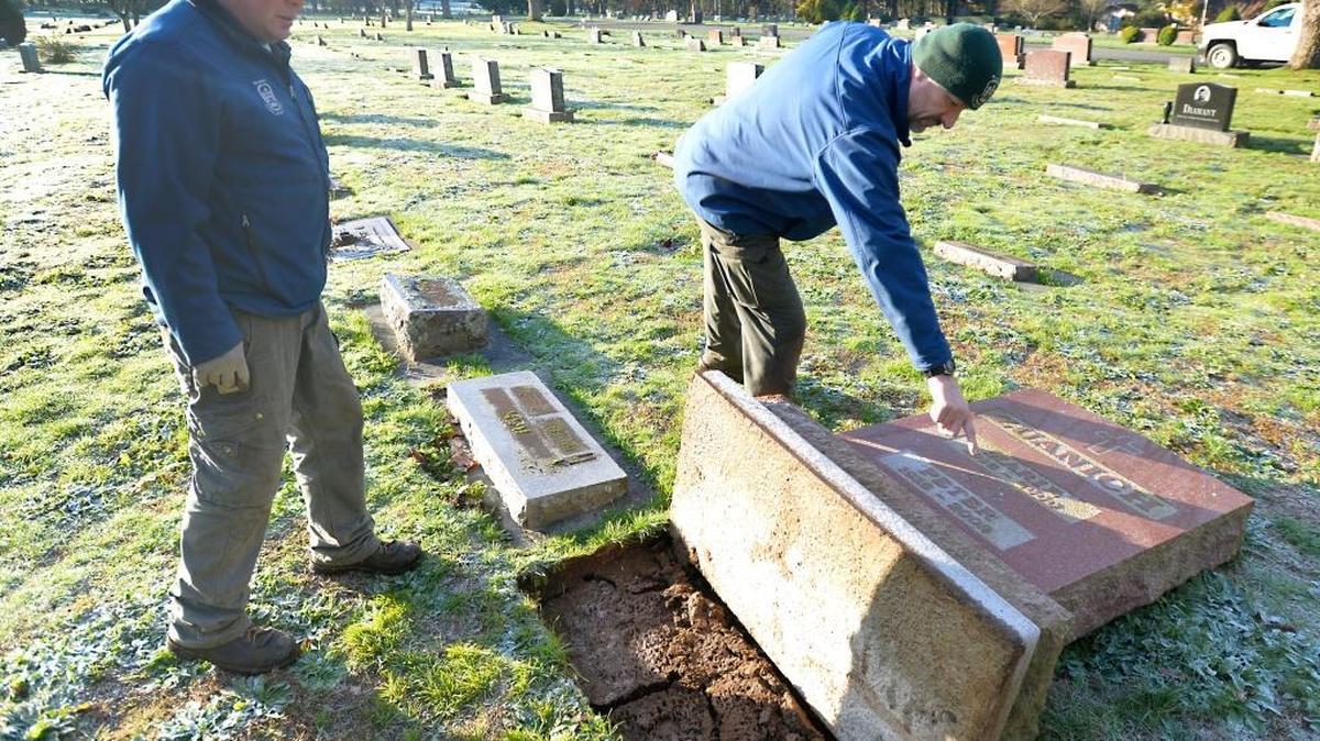 City of Bellingham Parks and Recreation worker Bradley Lease, left, and technician Troy Cummings look at the Zuanich headstone on Friday, Nov. 20, 2015. It was one of more then 40 headstones knocked down Wednesday night by vandals at Bayview Cemetery.
