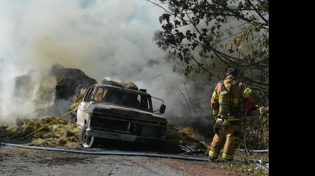 
A firefighter looks over a Ford F-350 pickup that caught fire Friday afternoon, July 17, igniting the bales of hay it was hauling along Old Samish Road.
