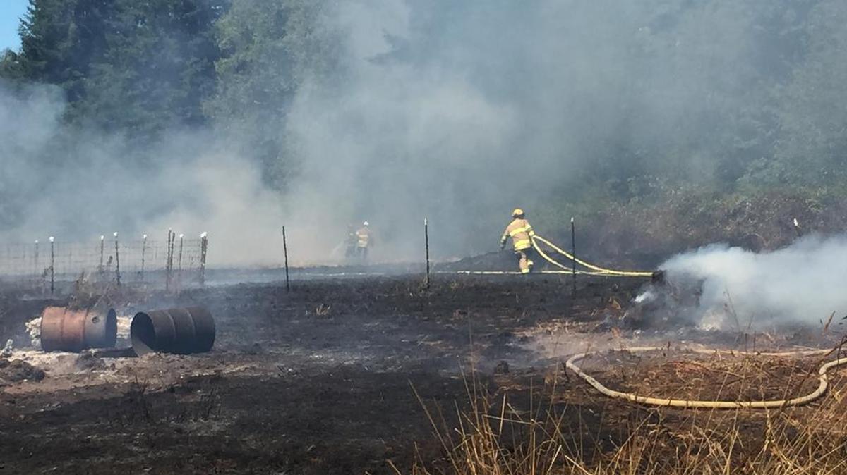 Firefighters clean up a grass fire at 3370 Sweet Road near Blaine on Tuesday morning, Aug. 4. The fire was knocked down within 30 minutes after burning two acres, a small shed and an old car, said acting North Whatcom Fire Chief Bill Pernett.
