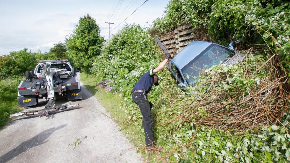 Brandon Rothwell with Johnson’s Towing cuts away brush from a car that went over a ledge near South Bay Trail in Bellingham on Friday, May 27, 2016. Police were searching for the driver, who had fled the scene.