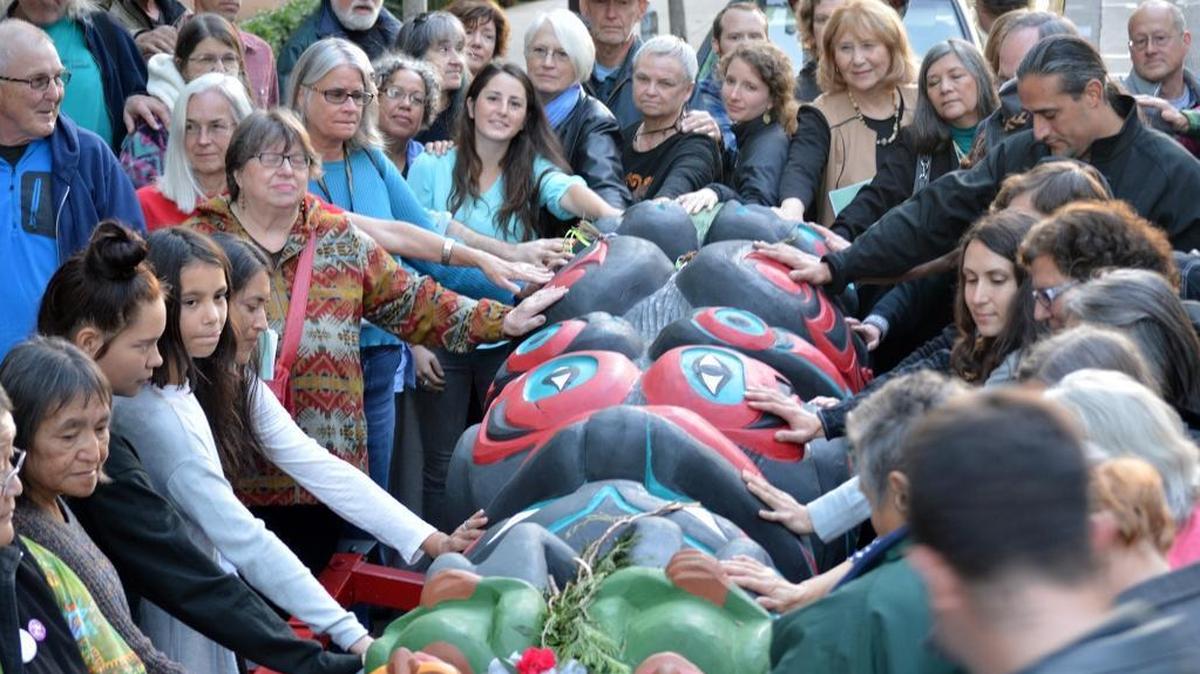 A crowd lays their hands on a totem pole bound for the Carnegie Museum of Natural History during a blessing event Monday evening, Oct. 16 in Vancouver, Washington. The pole is a symbol of tribal resistance to several fossil fuel projects in Washington state.