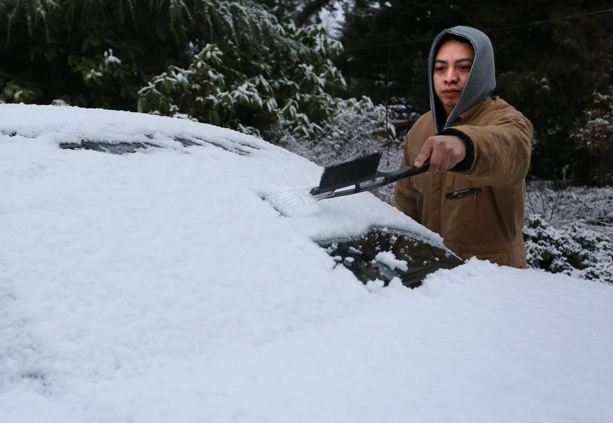 A driver brushes snow off his car in Bellingham. Police recommend removing snow and ice from your vehicle and making sure all lights are visible when you have to drive in the snow.