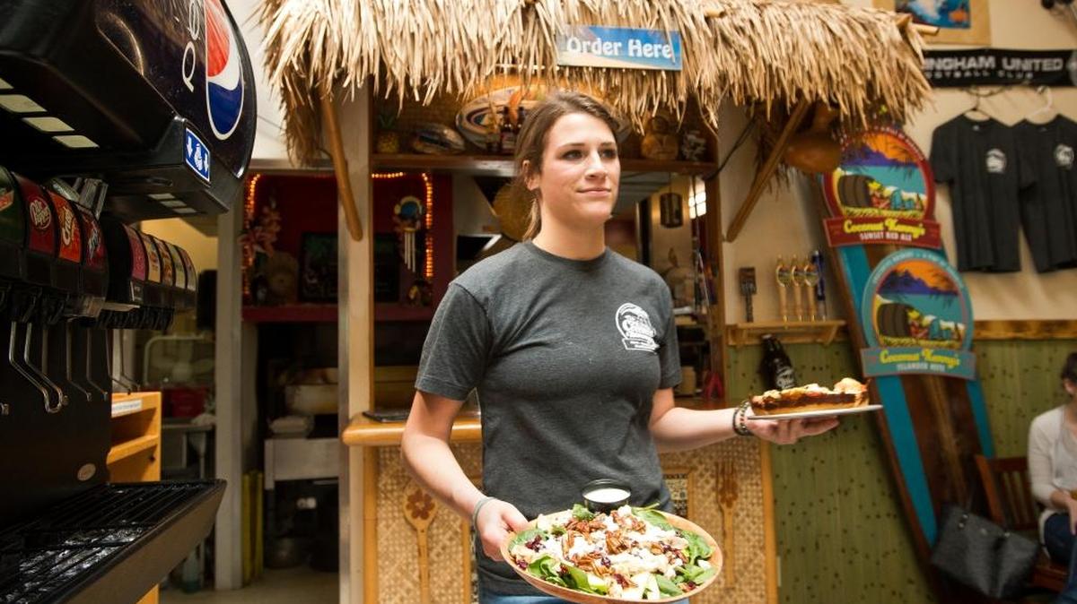 Employee Jillian Segaline carries a Catalina salad and a Kailua Kona pizza to customers at Coconut Kenny’s on Thursday, May 20, in Bellingham, Wash. Another Coconut Kenny’s restaurant is expected to open in Lynden in mid-summer.