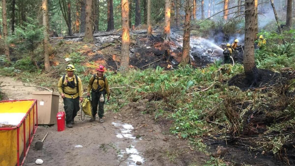 Firefighters walk past a water holding tank, left, as firefighters in the background douse lingering embers on Saturday.