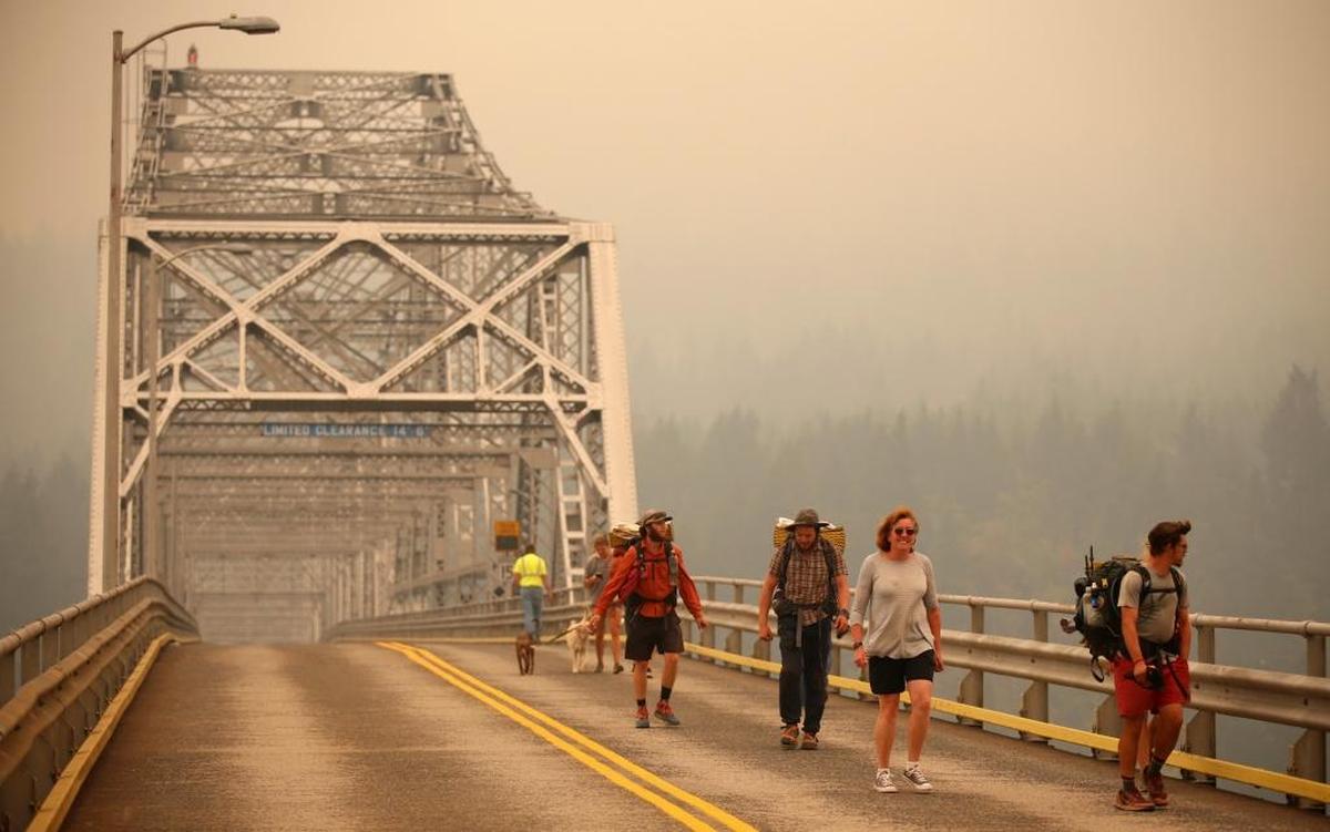 Pedestrians walk off the Bridge of the Gods, which spans the Columbia River between Washington and Oregon states, as smoke from the Eagle Creek wildfire obscures the Oregon hills in the background near Stevenson, Wash., Wednesday, Sept. 6, 2017. The Eagle Creek fire continues to burn on the Oregon side of the river near the town of Cascade Locks, Ore. Officials closed the bridge to pedestrians and onlookers after this photo was taken.