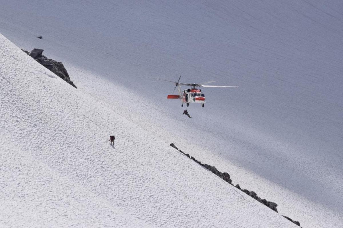 A Navy search and rescue team member from Whidbey Island Naval Air Station is lowered to help an injured climber from the slopes of Mount Baker on Saturday, August 19.