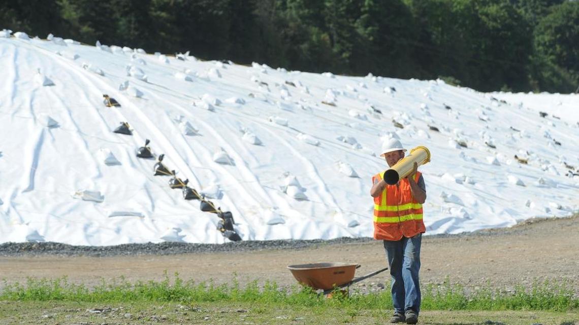 Pacific Northwest Probe & Drilling worker Jon Root hauls a cover for a monitoring well at the old Cornwall Avenue Landfill along Bellingham Bay in 2012. Behind Root is 47,000 cubic yards of fill material that was dredged from the Squalicum Harbor marina and is covered with a waterproof tarp.