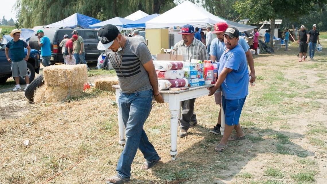 Farmworkers move a table and some supplies from an old kitchen area to a new kitchen area at their camp on Friday, Aug. 11, near Sumas.