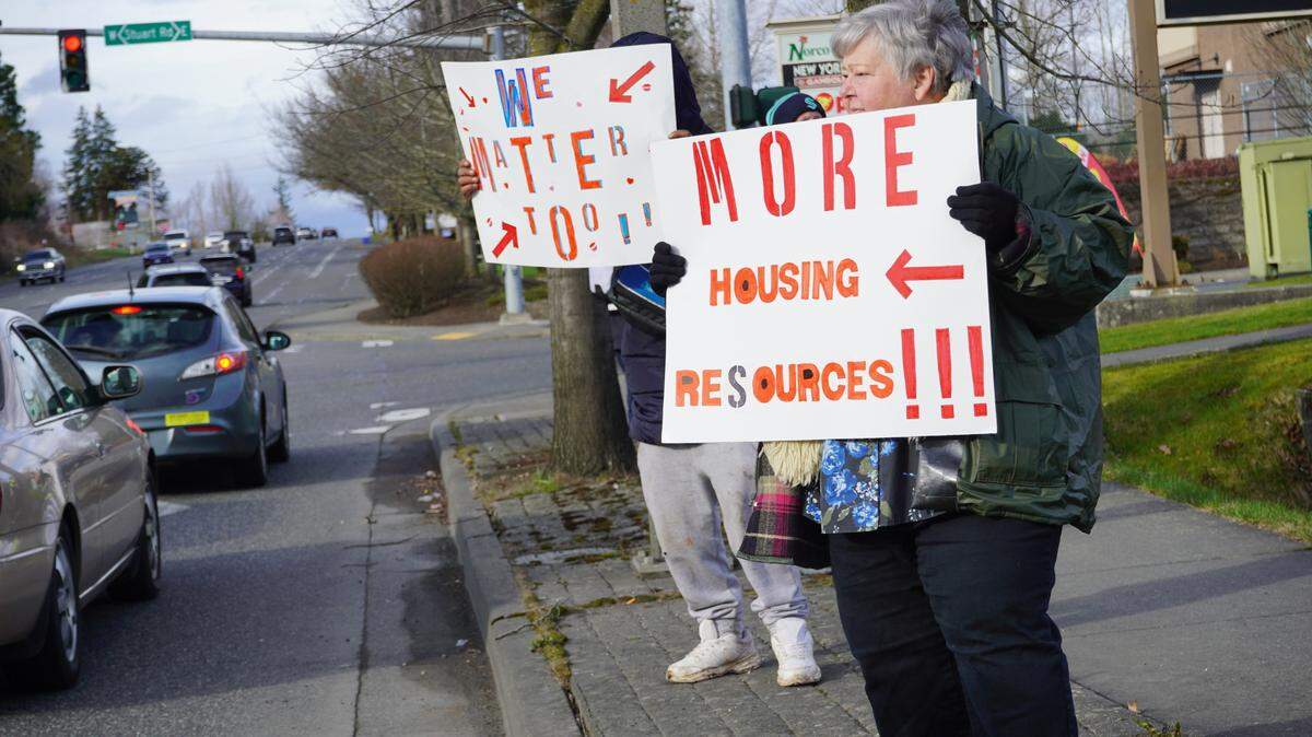 People hold signs saying, ‘We matter too,’ and ‘More housing, more resources,’ along Meridian Street on March 9, 2024, to protest the impending clearing of the encampment behind Walmart in Bellingham, Wash.