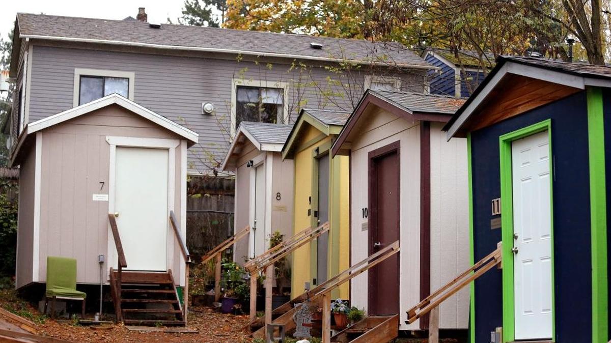 A row of tiny houses at a homeless encampment stand in view of a full-size home behind, in Seattle. Tiny homes could be the solution to all kinds of housing needs, offering warmth and security for the homeless, an affordable option for expensive big cities and simplicity for people who want to declutter their lives. However, that seemingly broad support fails to translate into acceptance when tiny home developers try to build next door.