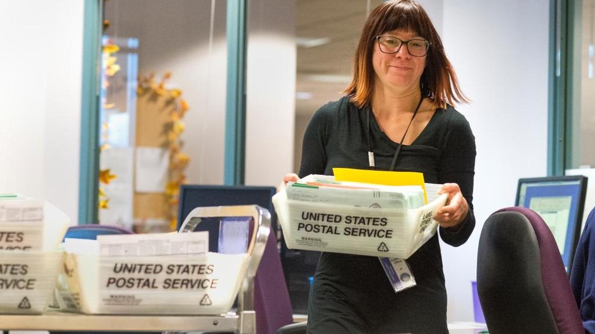 Election worker Jennifer Nichols carries a box of ballots after completing a signature verification process on Thursday, Oct. 22, at the Whatcom County Auditor's Office in Bellingham, Wash. Voters mailing ballots need use only one stamp as the county will pay for the extra postage required on the heavier-than-usual ballots.