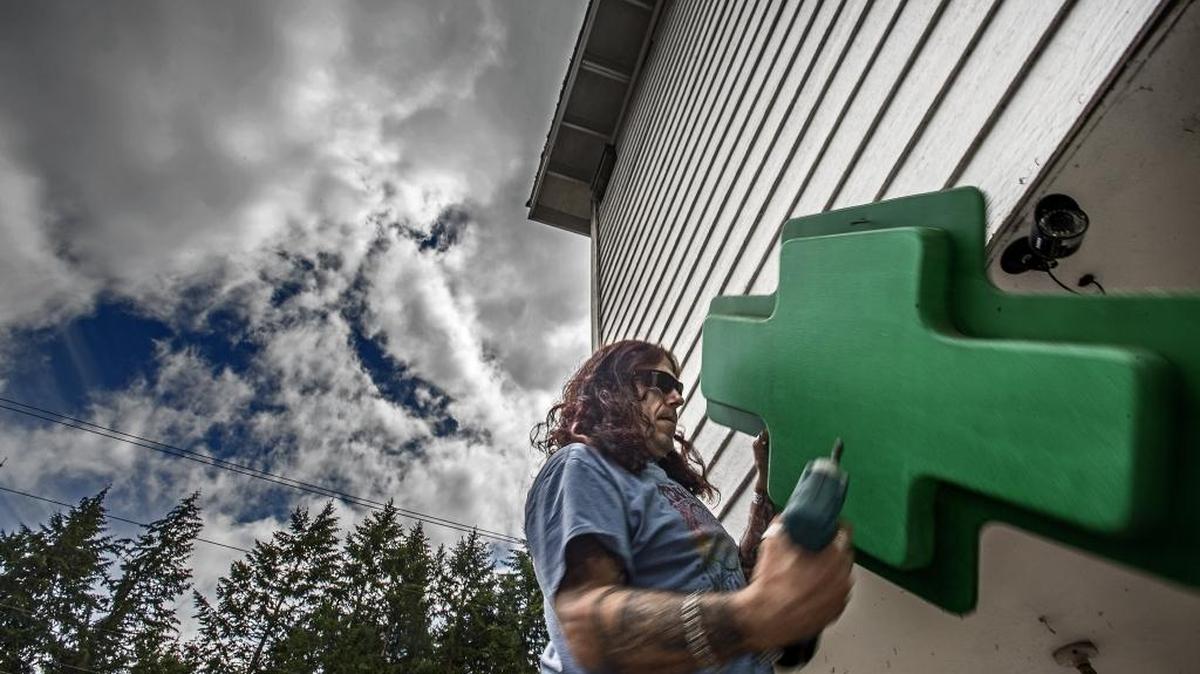 Chad Oliveira takes down one of the signs Tuesday outside the KP Healing Center on state Route 302 on the Key Peninsula Tuesday, June 21, 2016, in preparation for the shop closing at the end of the month. Washington state will be enforcing the merger of recreational and medicinal marijuana shops starting on July 1.